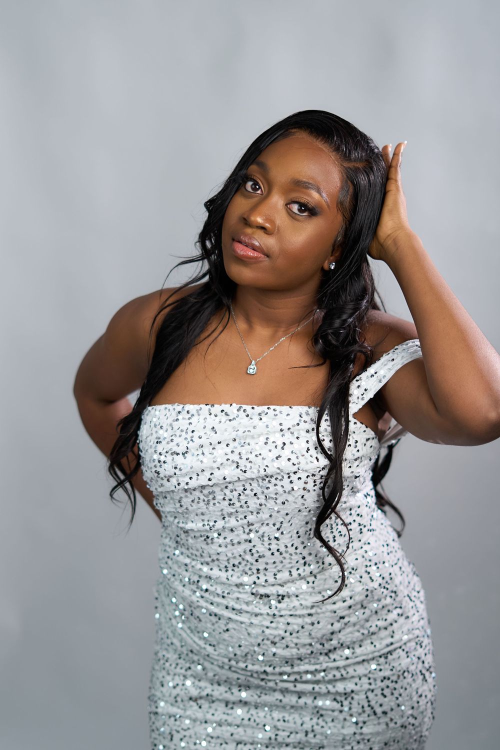 Woman wearing a sparkly silver sequined dress posing against a grey background.