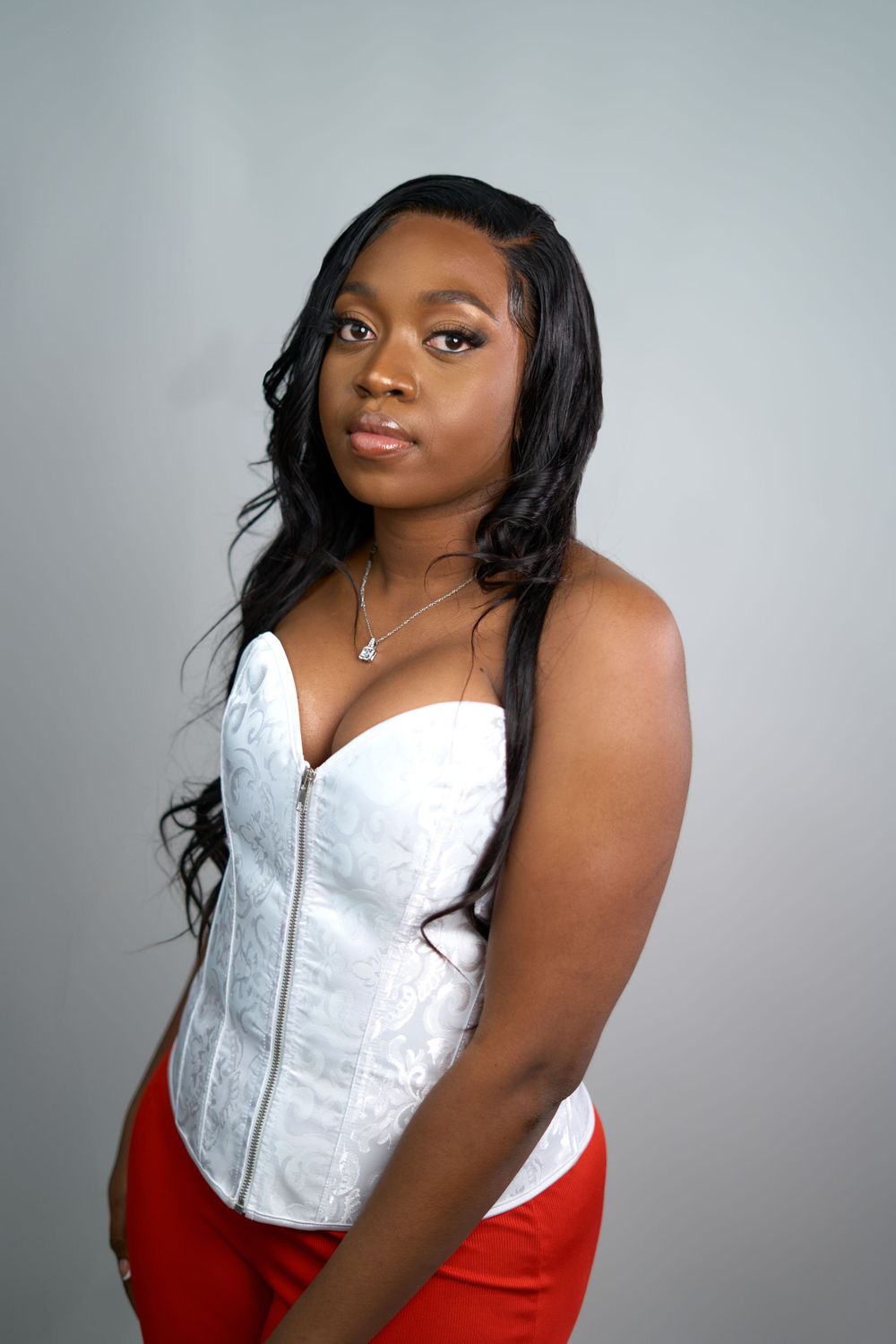 Portrait of woman in white structured corset and red pants against studio backdrop.