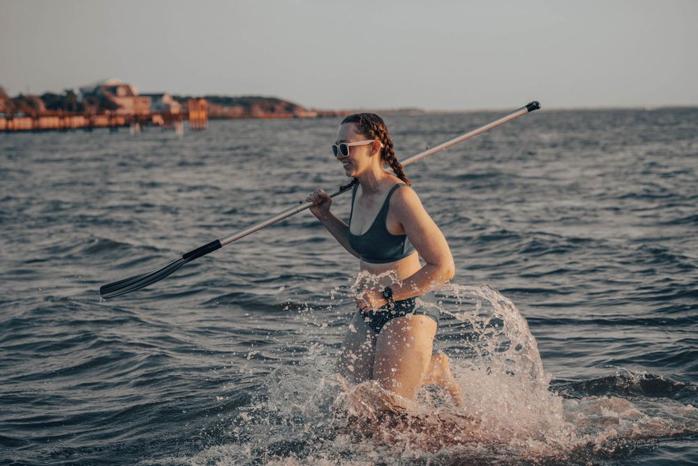 Paddleboarder creates splash while navigating through ocean waves at dusk.