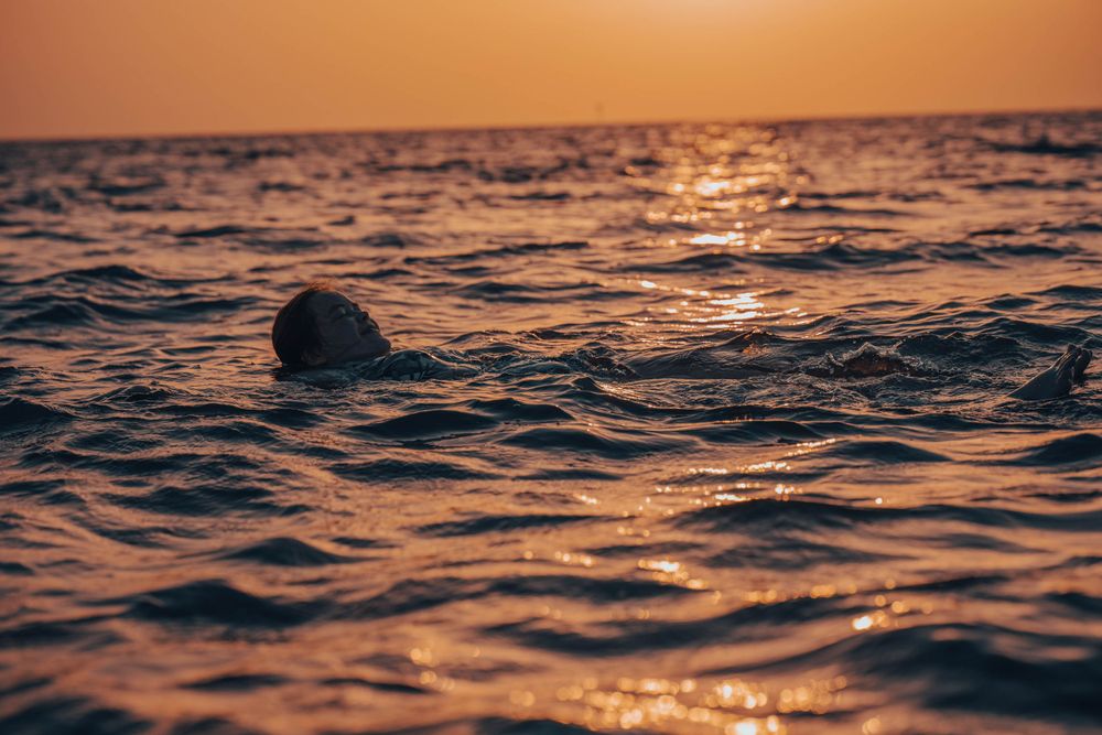 Single head visible above ocean waves during golden sunset.