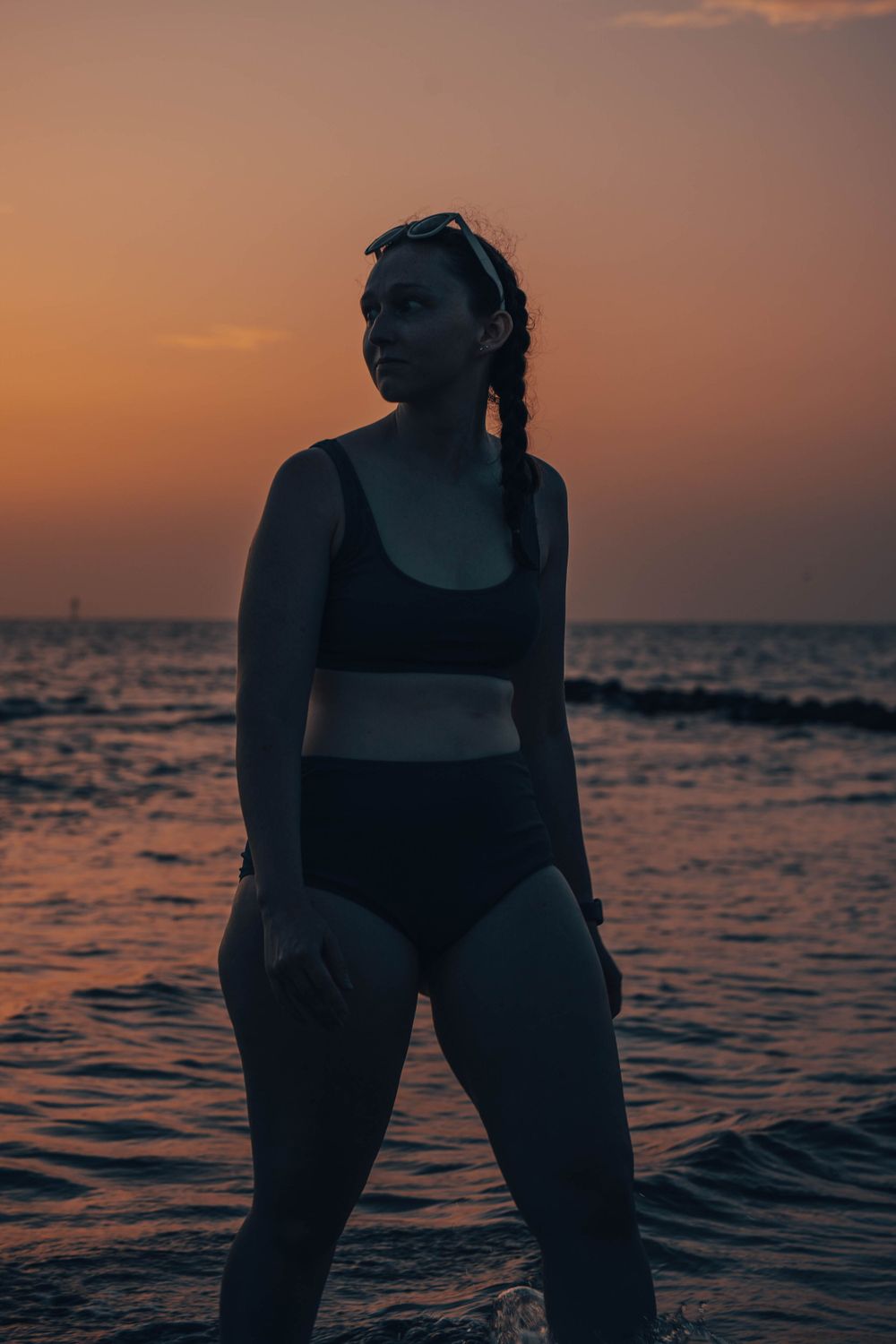 Person in black swimwear poses in ocean waves during sunset.