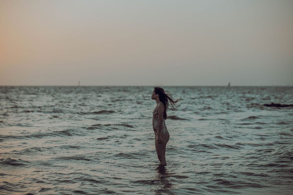 Silhouette of person standing in ocean waves during sunset with arms outstretched.