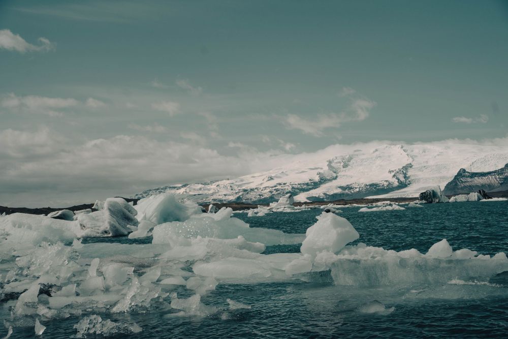 Dramatic landscape of floating ice chunks in glacial waters against snow-capped mountains.