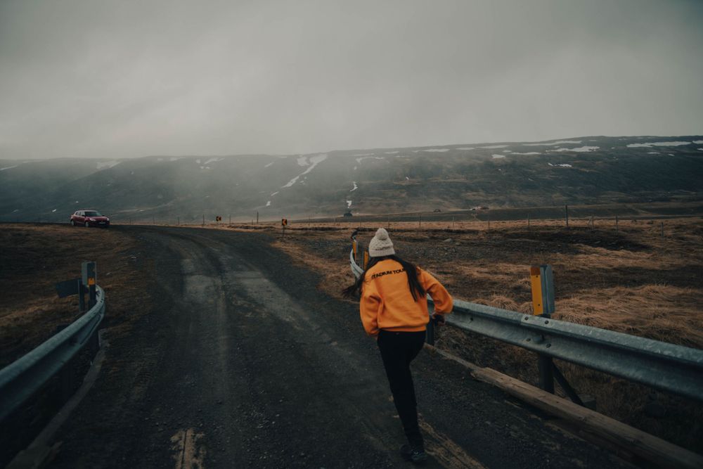 Explorer in yellow jacket walking along curved mountain road at dusk.
