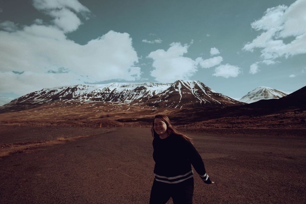 Traveler poses against backdrop of snow-capped mountain under cloudy sky.