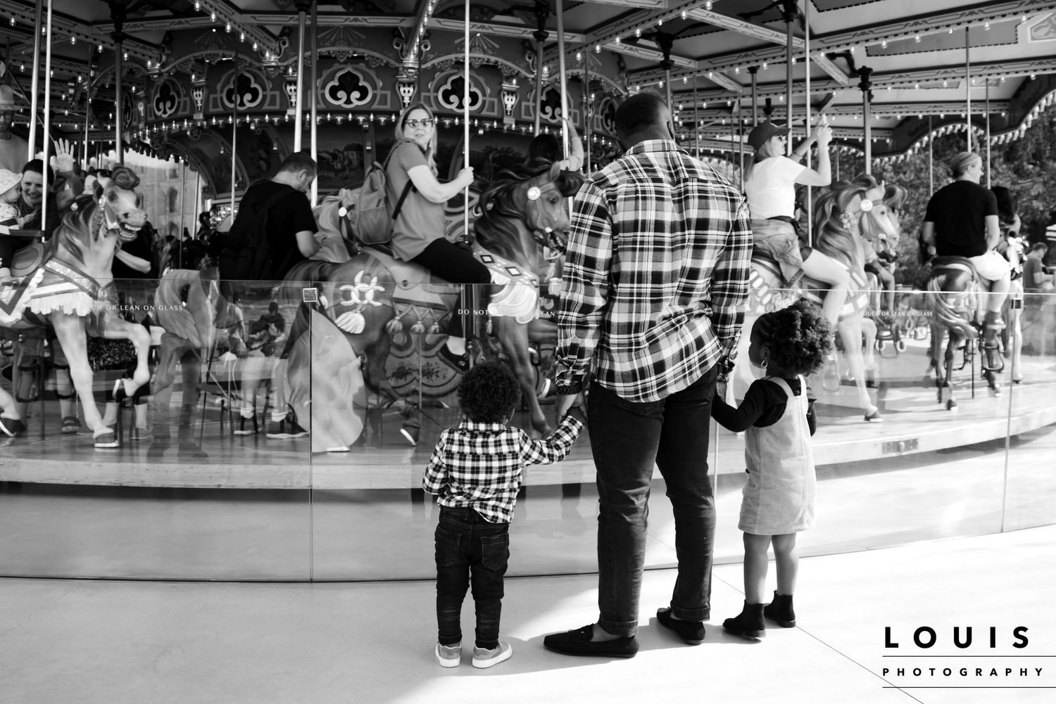 A parent and children watch carousel horses at an indoor amusement park ride.