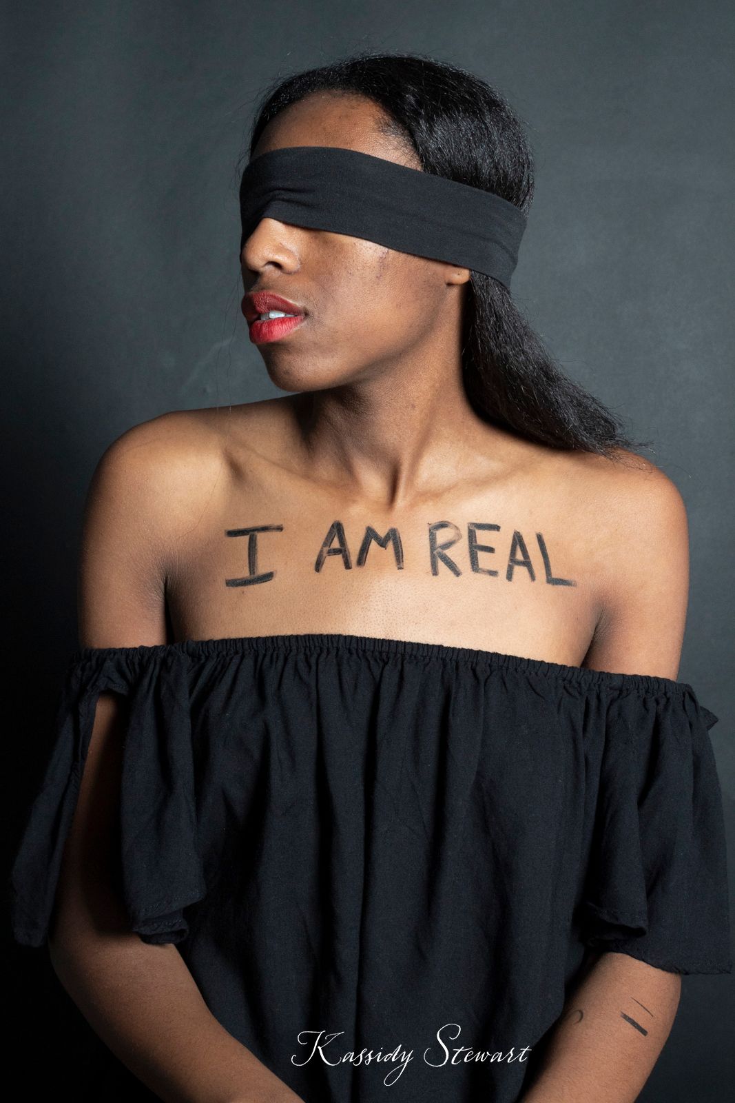 A model wearing a blindfold with the words "I am real" written on their chest.