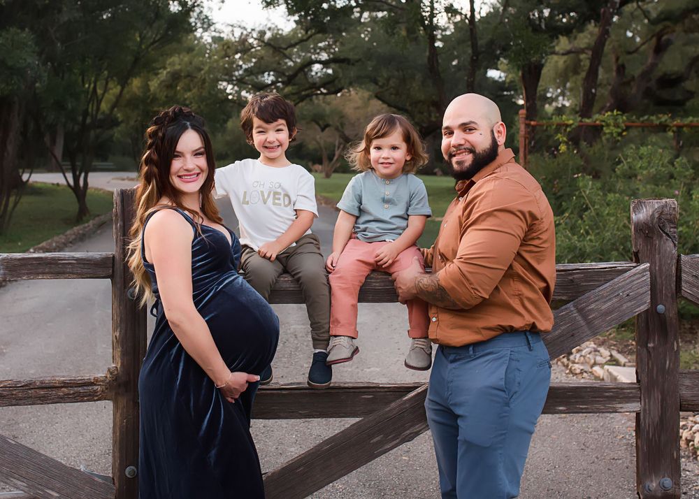 Family poses together on a rustic wooden fence in an outdoor autumn setting.