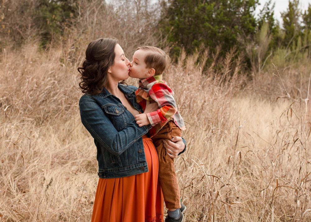 Parent and child share tender moment in tall autumn grass.