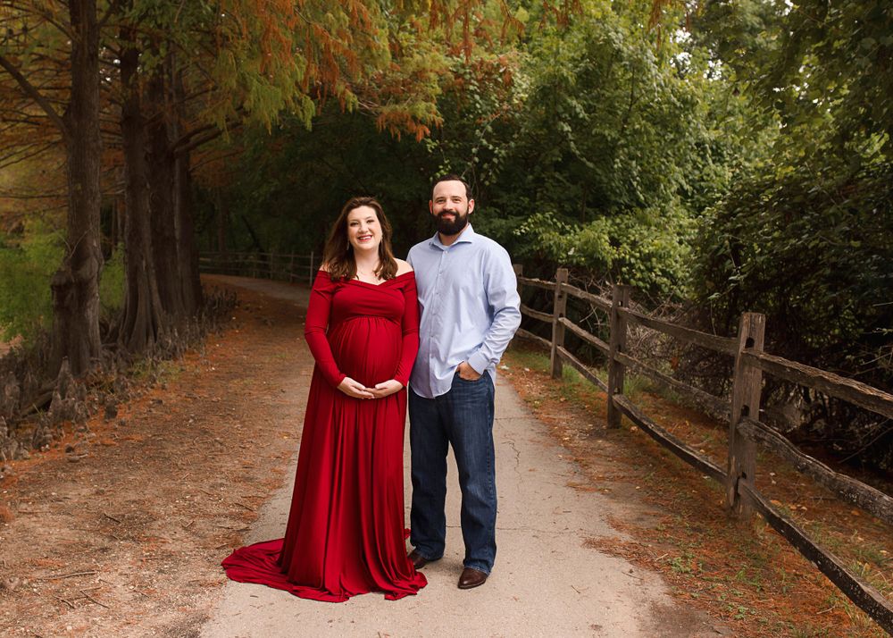 Outdoor maternity portrait on wooded path with couple in casual attire.