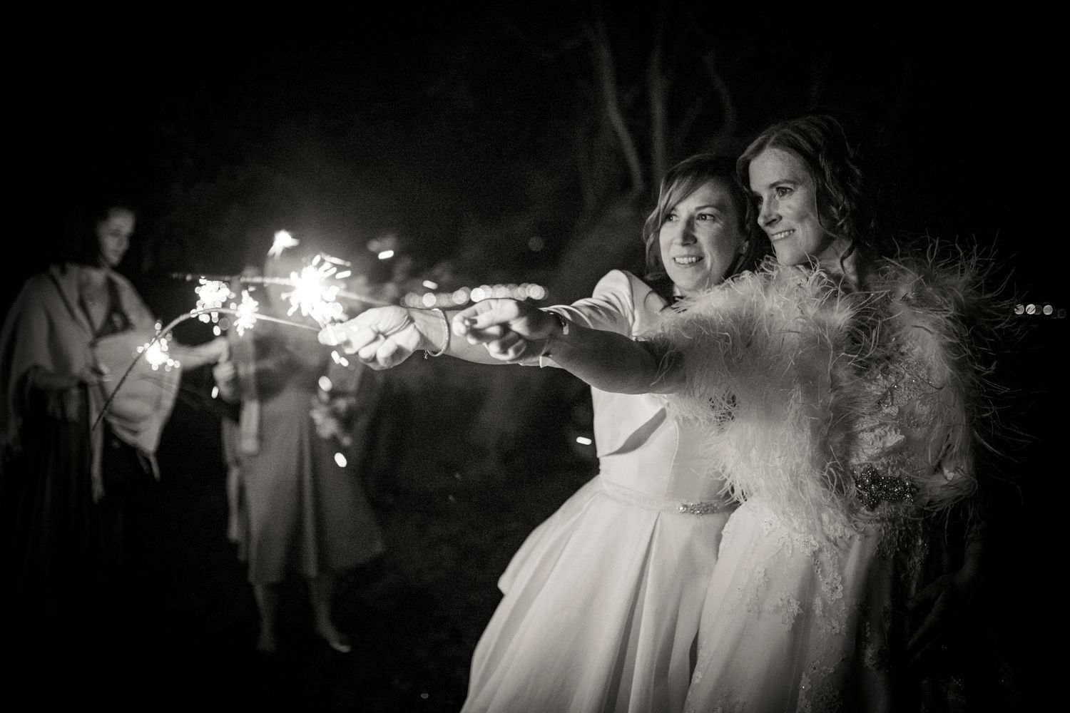 Dramatic nighttime portrait of newlyweds holding sparklers against a dark background.