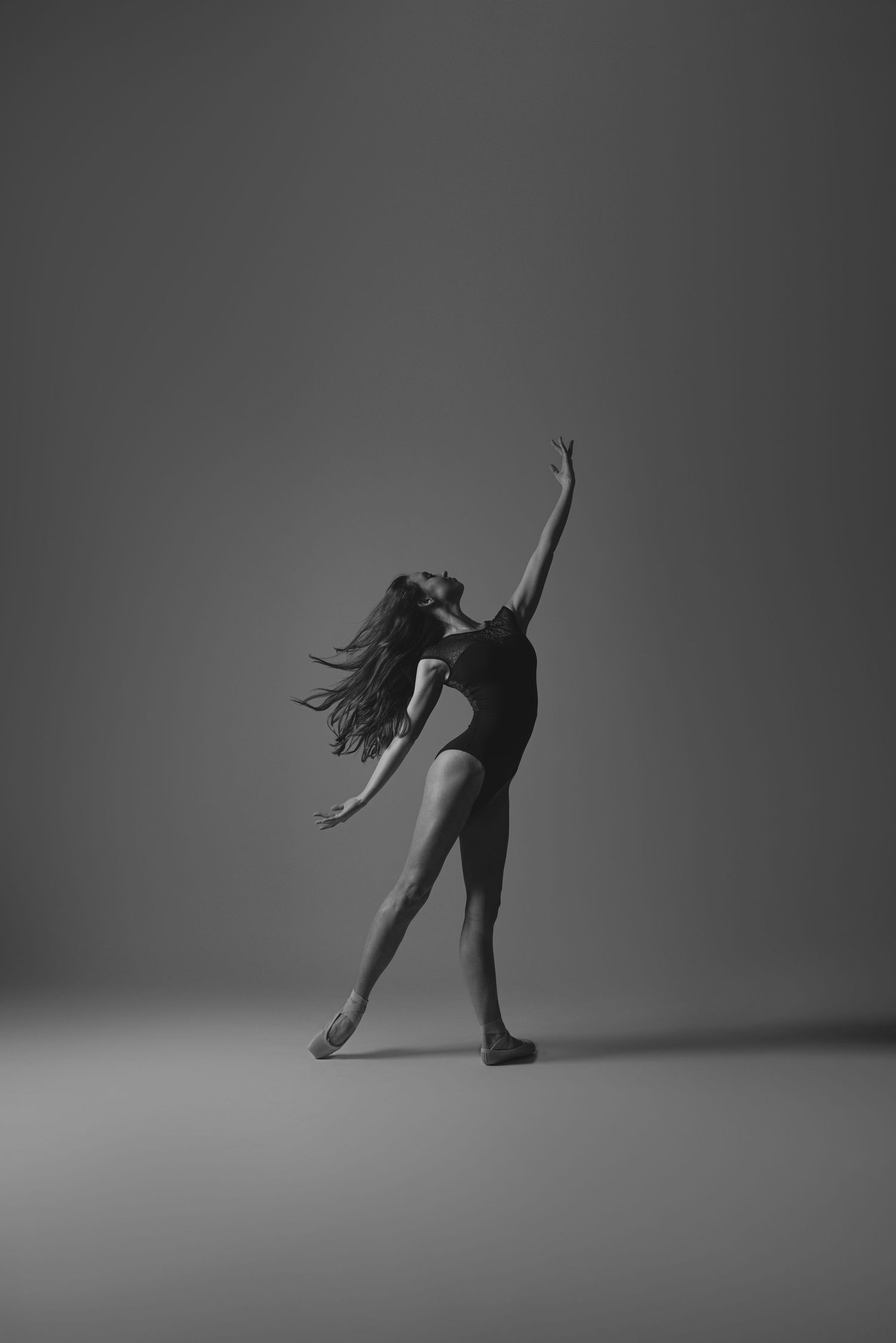 Black and white image of dancer in flowing movement with dramatic hair motion against simple backdrop.