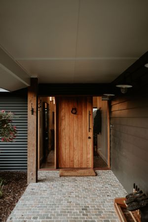 Modern entryway with wooden door and brick paved landing.