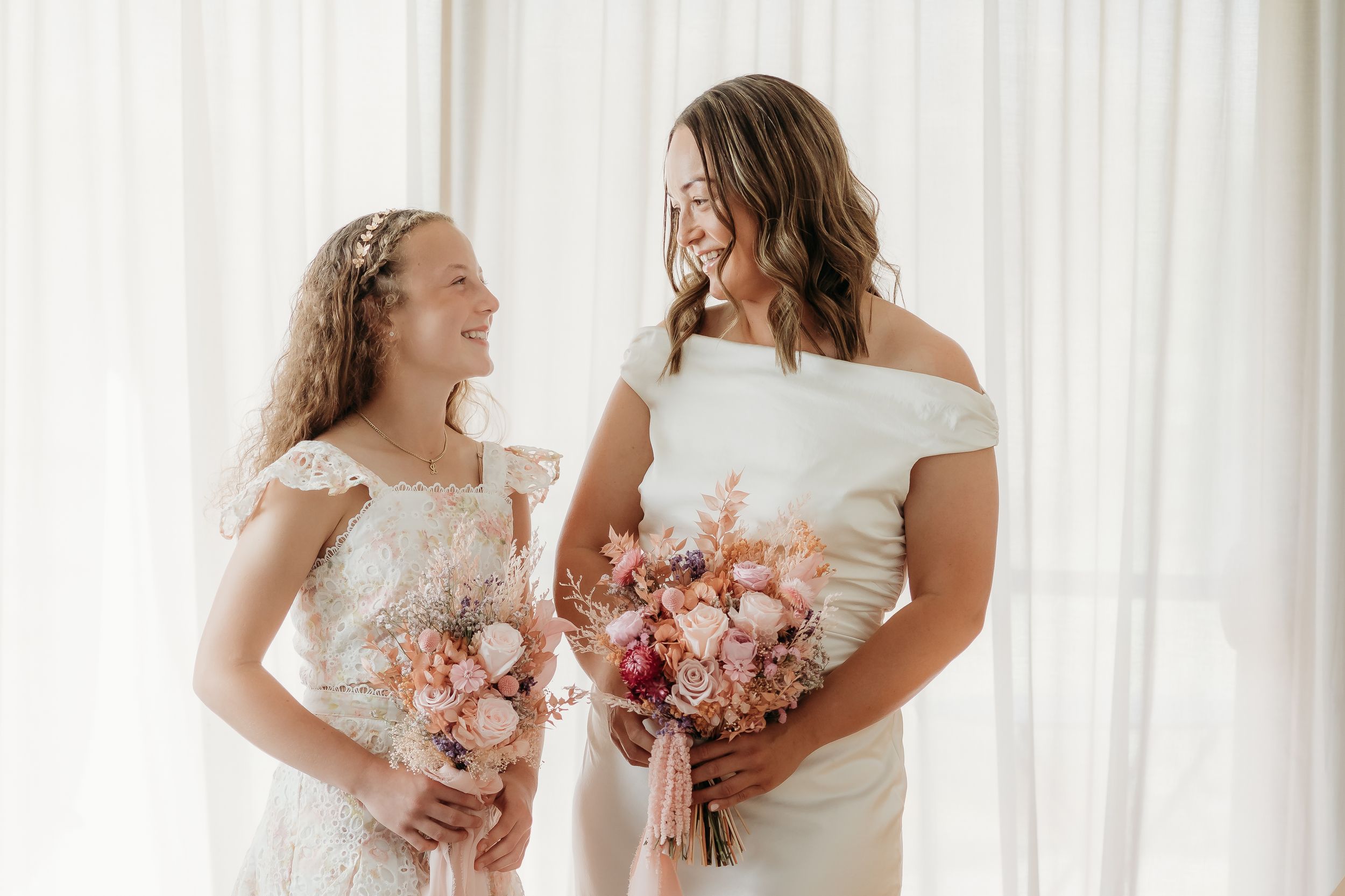 Two figures in white dresses holding matching floral bouquets against a light backdrop.