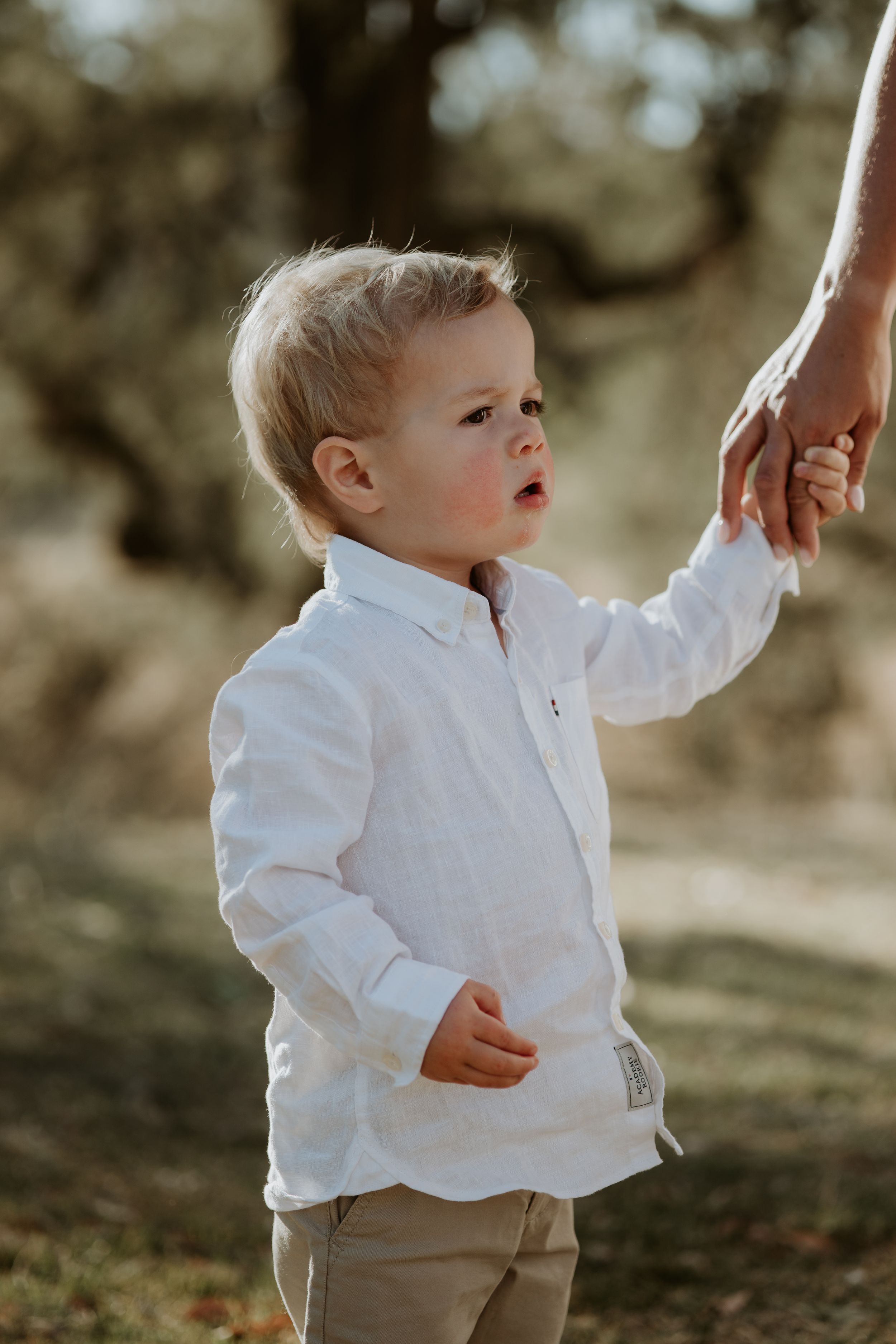 Toddler in white dress shirt walking outdoors in golden sunlight.