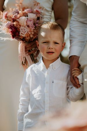 A young attendee in white dress shirt holding a pink and burgundy floral bouquet.