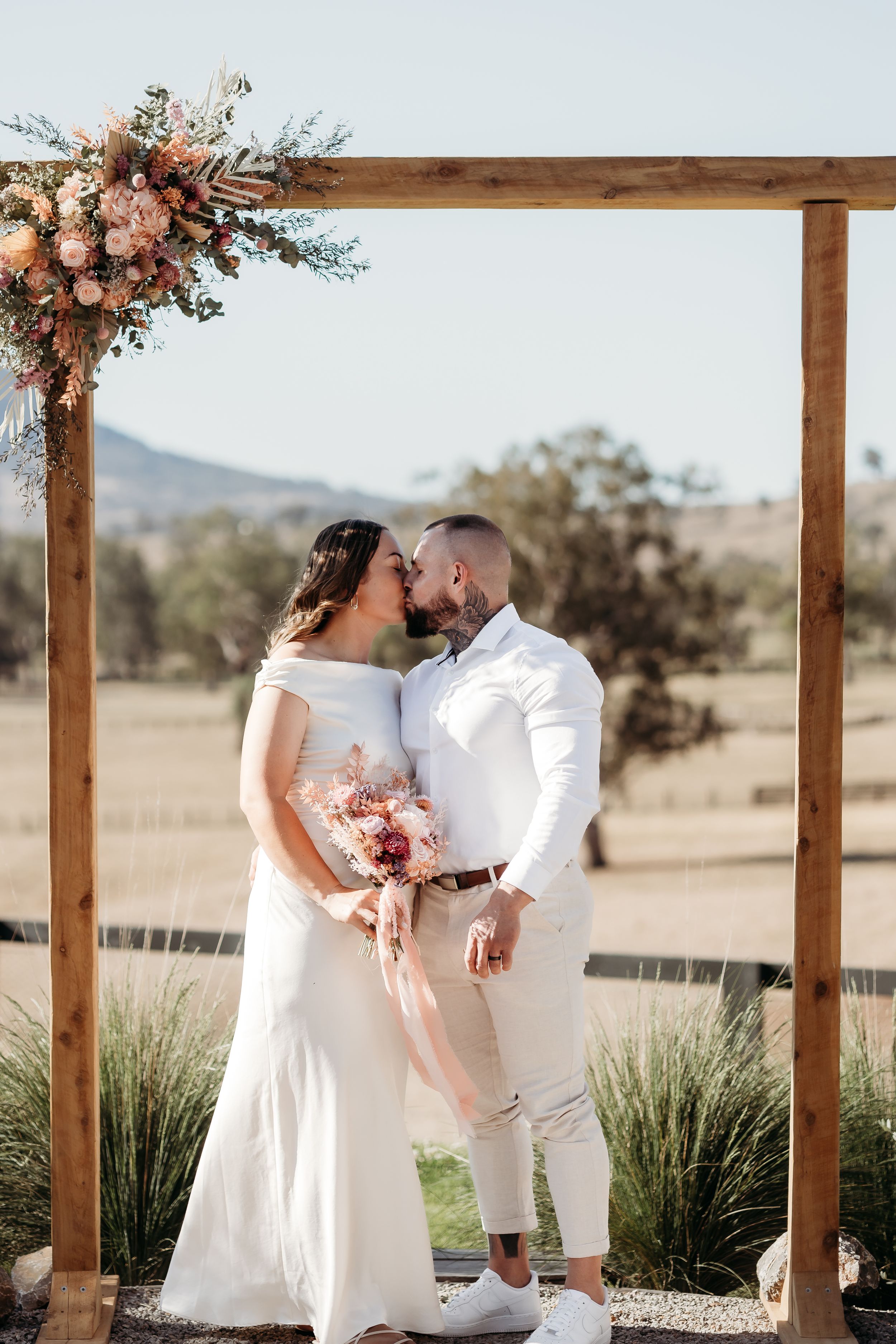 Beautiful countryside wedding scene with rustic wooden pergola and floral decor.
