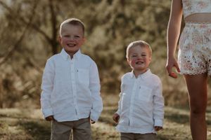 Children in white clothing smile and play during outdoor family photoshoot.