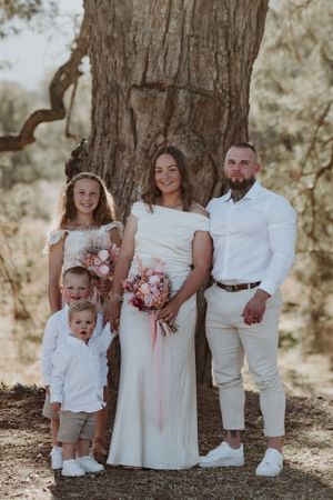 Family portrait against large tree trunk in coordinated white and pink outfits.
