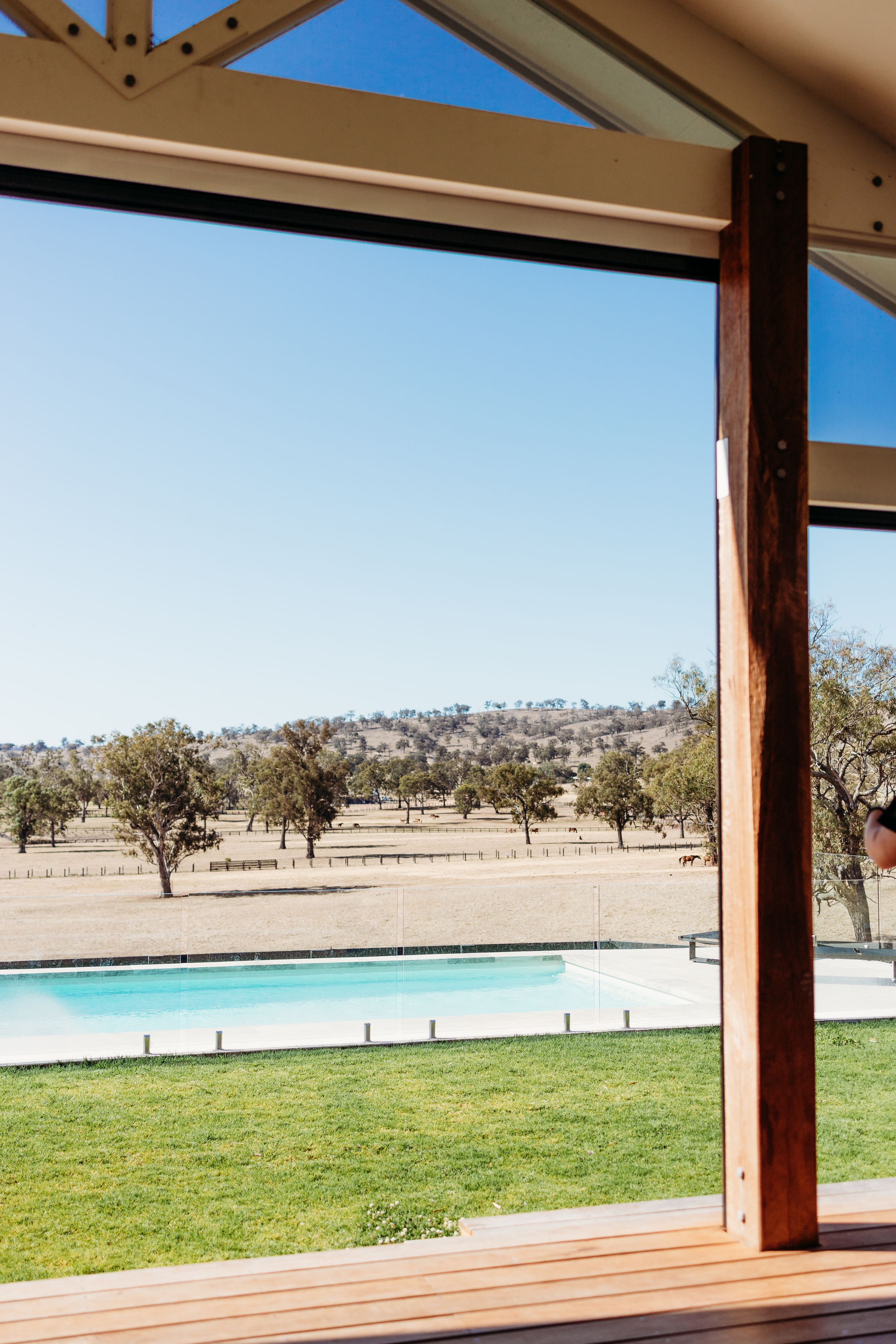 A modern outdoor venue with wooden beams overlooking a swimming pool and rural landscape.