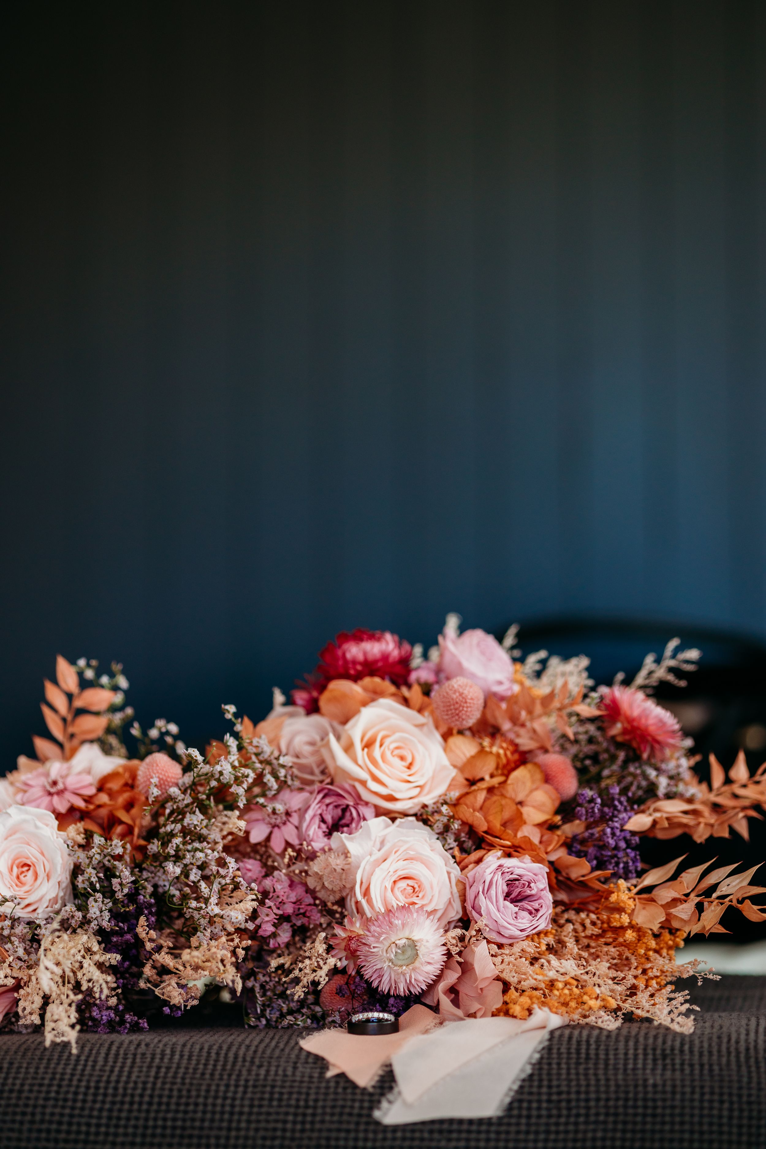 A romantic floral arrangement with pink and peach roses against a dark background.