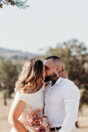 Romantic outdoor wedding photoshoot with peach floral bouquet and rustic backdrop.