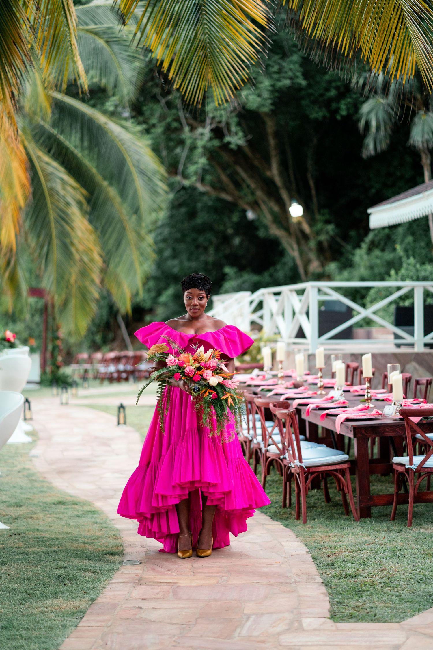 A vibrant pink dress stands out against a tropical wedding reception setup with palm trees.