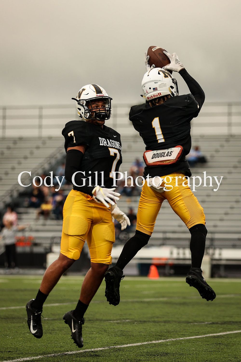 Two football players in black jerseys and yellow pants practice catching drills on the field.