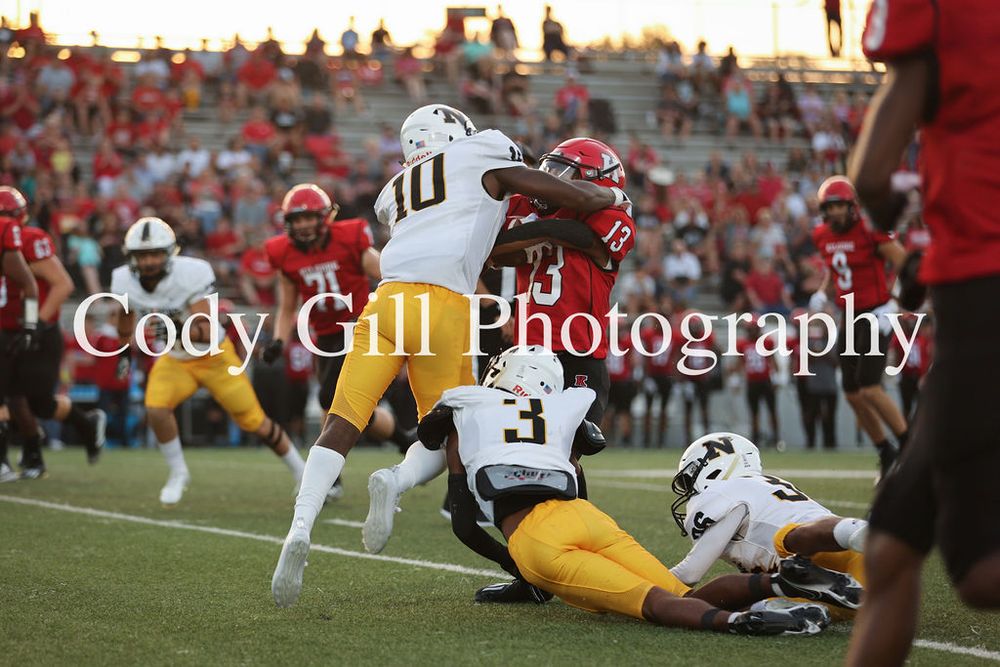 Football players in red and yellow uniforms tackle during a competitive game on the field.