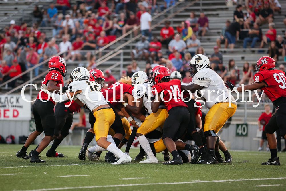 Football players in red and yellow uniforms clash during an intense scrimmage at the line of scrimmage.