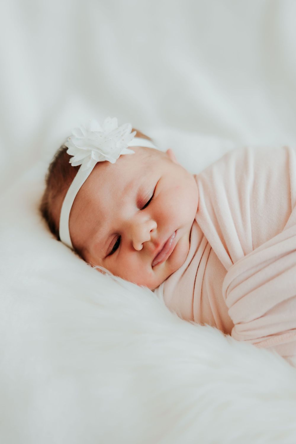 Peaceful sleeping newborn wrapped in pink with white headband.