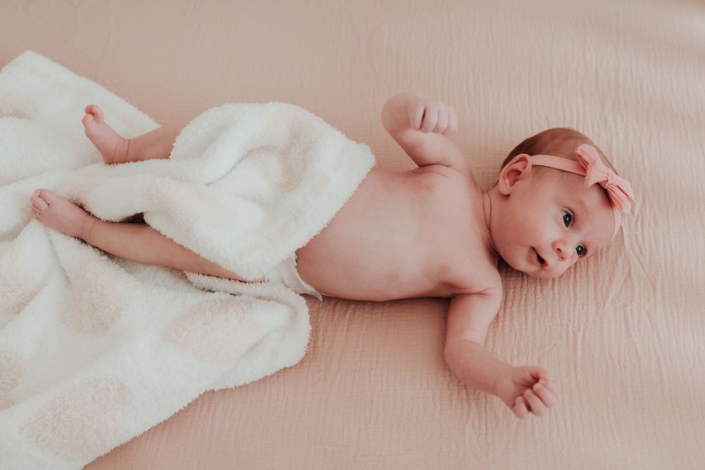 Newborn baby partially covered with white blanket lying on pink surface.