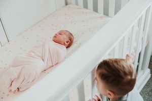Baby sleeping in white crib with pink bedding.