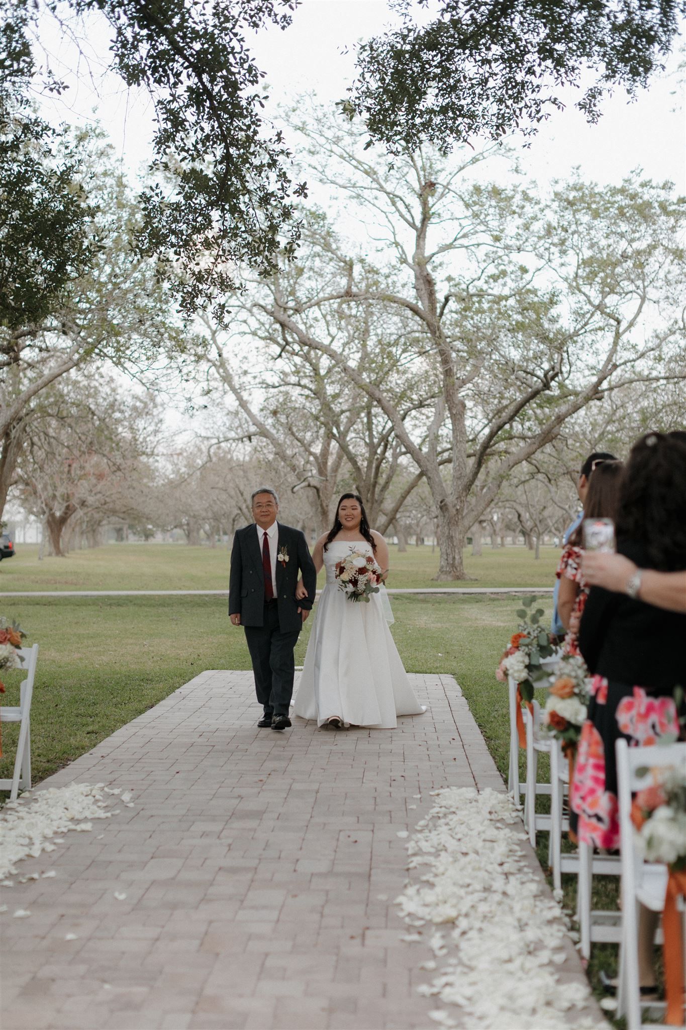 The wedding procession walks down a stone path lined with white flower petals.