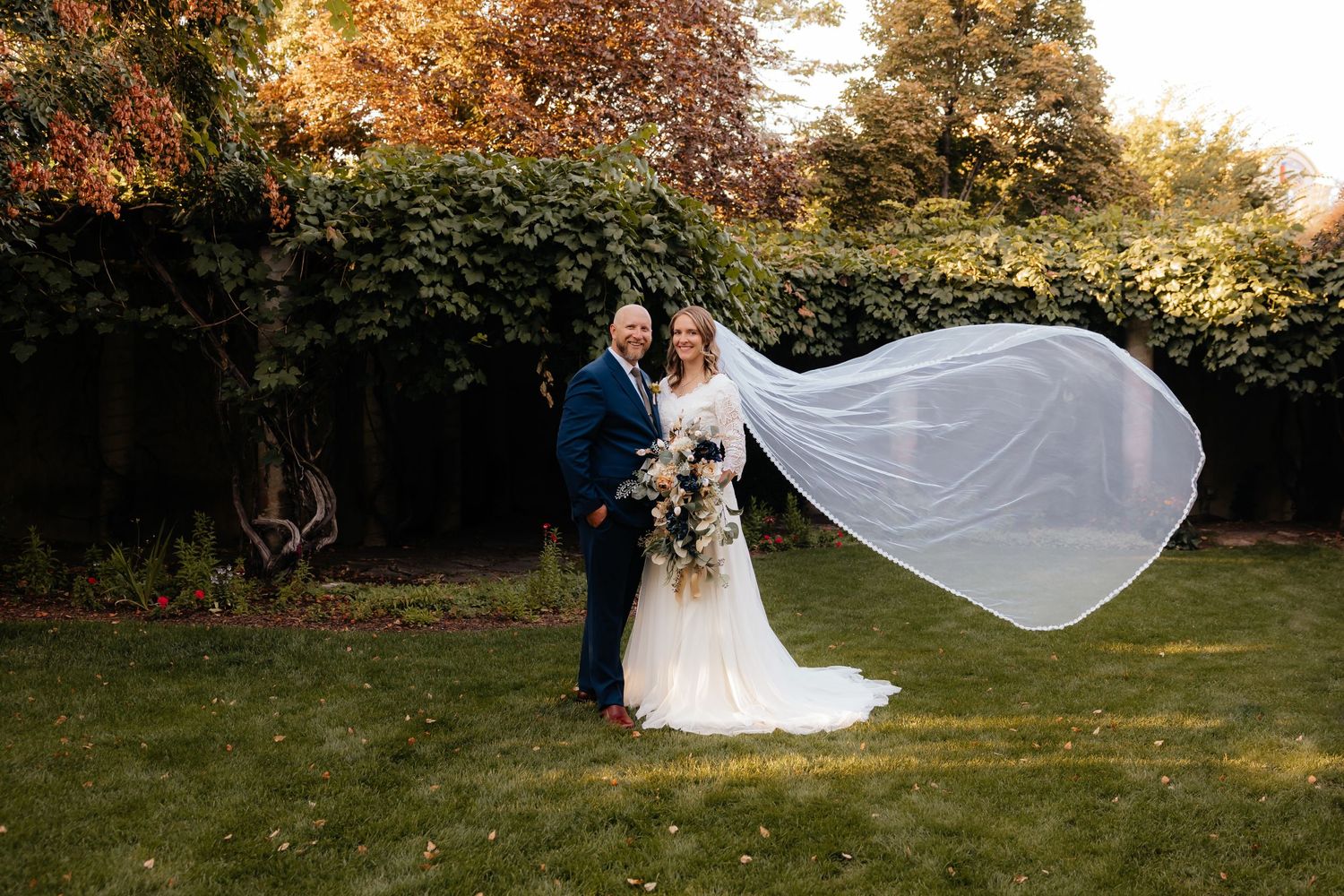 Bride and Groom standing in a garden with a long flowy veil