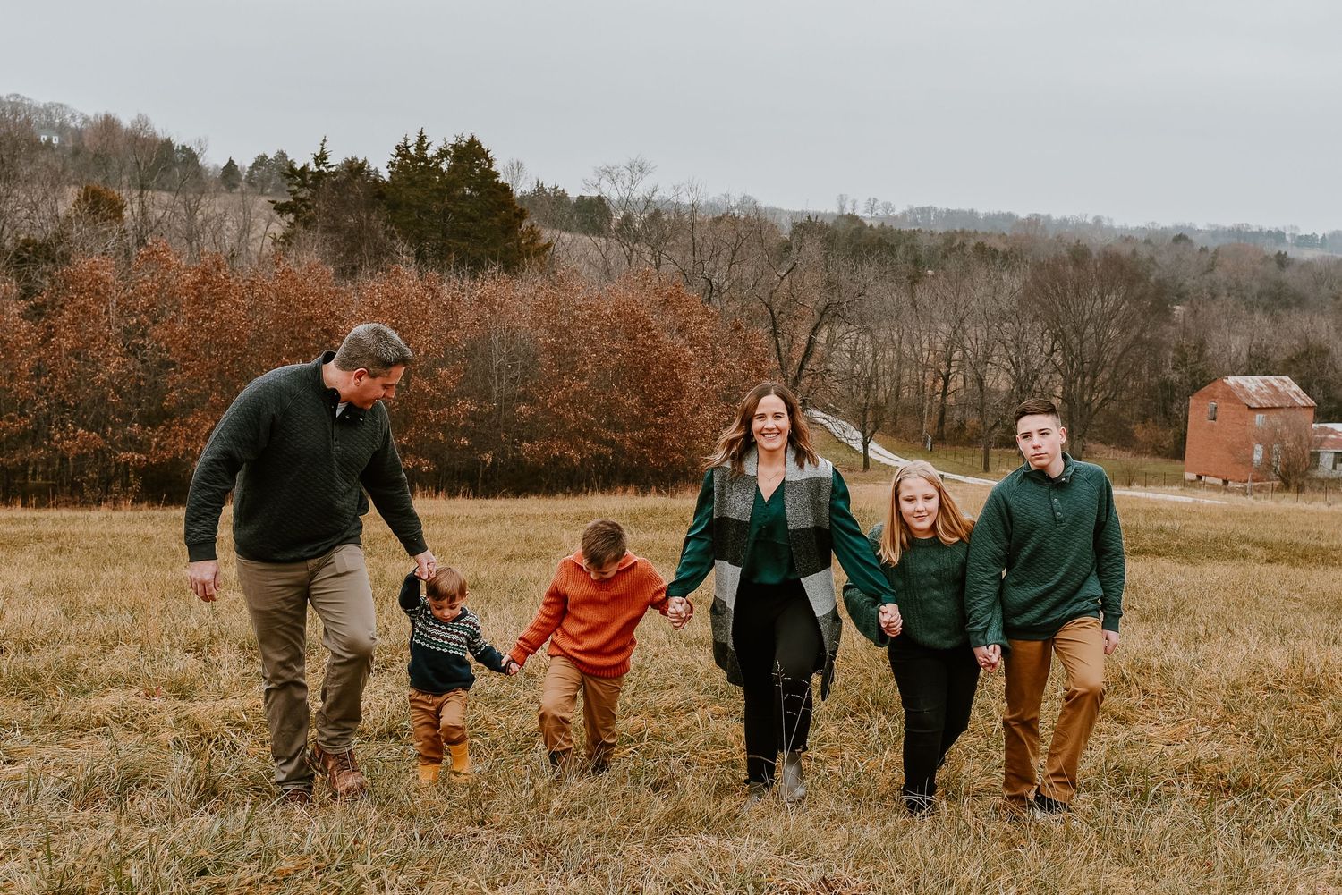 Family walking together hand in hand through an autumn field with rustic barn in background.