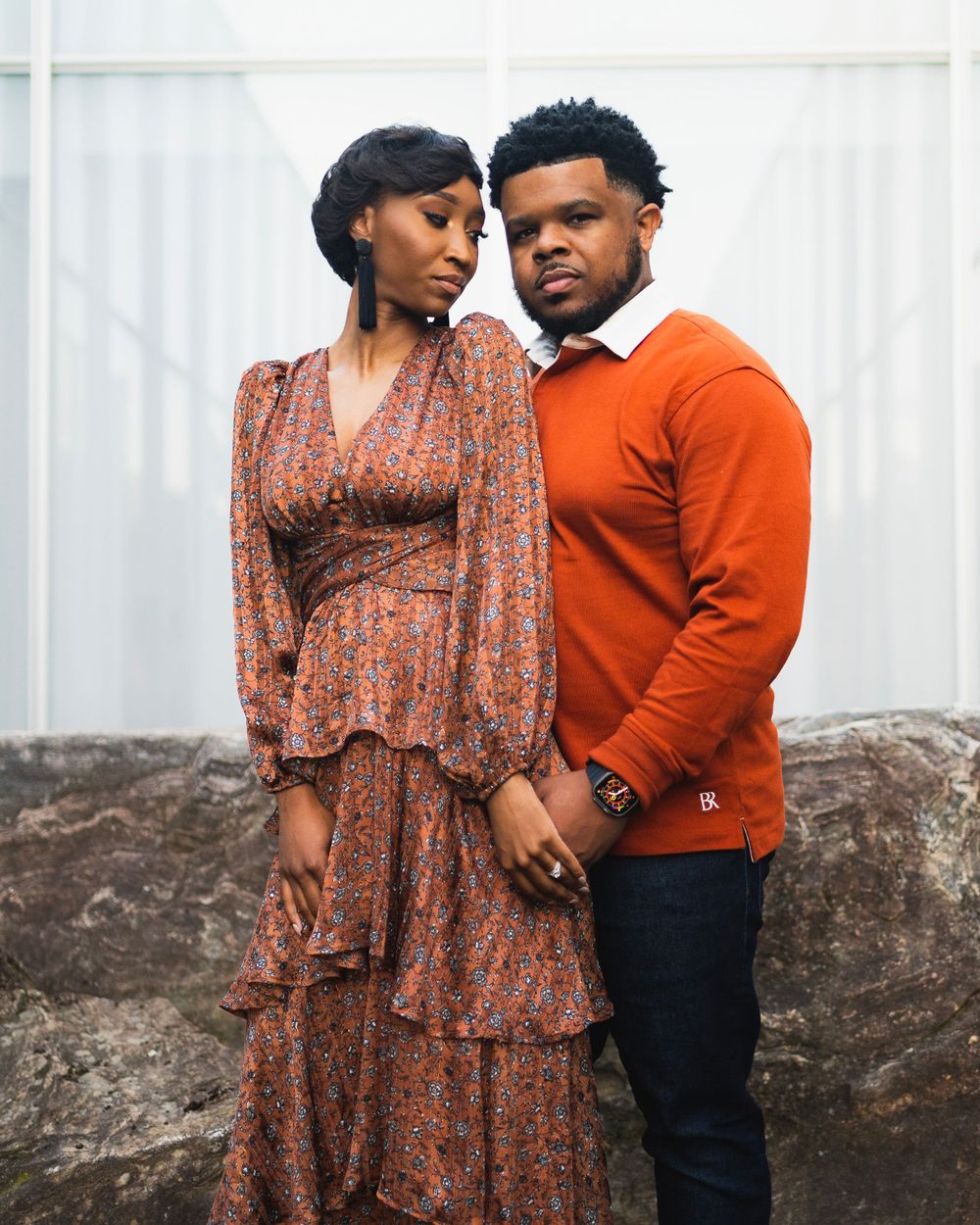 Couple in coordinated orange and brown outfits pose intimately against white backdrop.