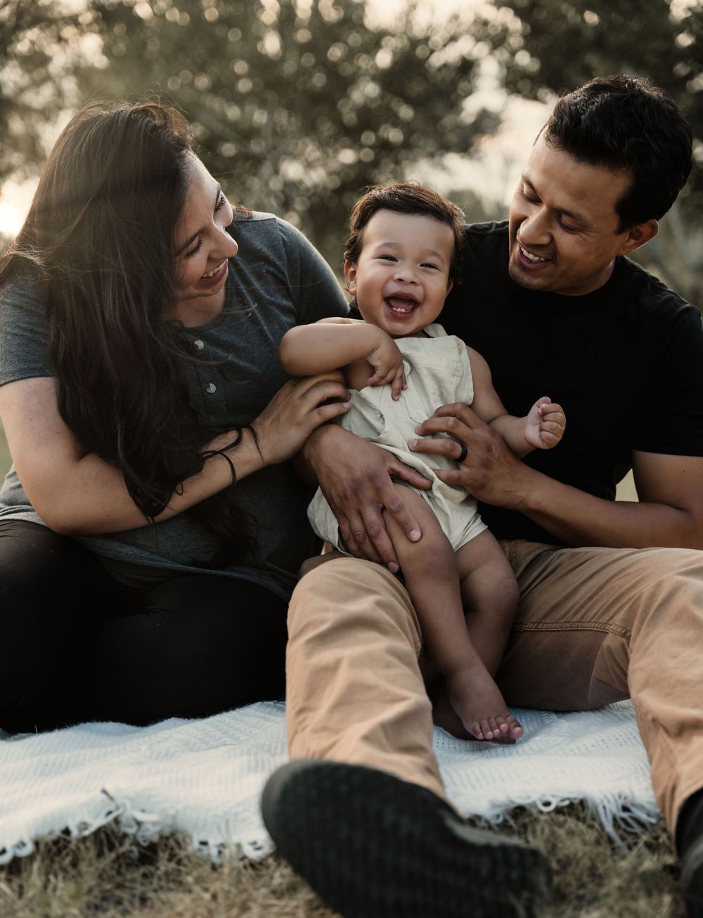 Happy family enjoying playful moment together on blanket outdoors during sunset photoshoot.