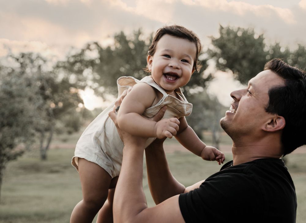 Joyful moment between parent and baby during outdoor sunset photoshoot.