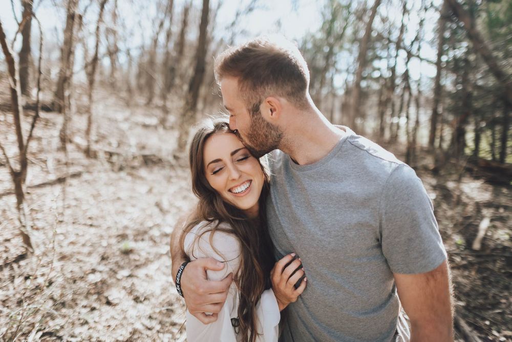 Couple sharing playful and intimate moments together in a wooded outdoor setting during a photo session.