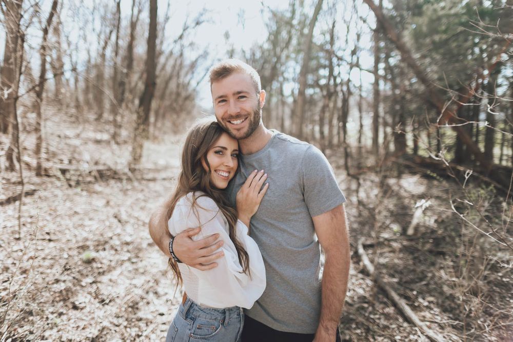 Romantic couple laughing and embracing while posing for casual photos in a forest setting.