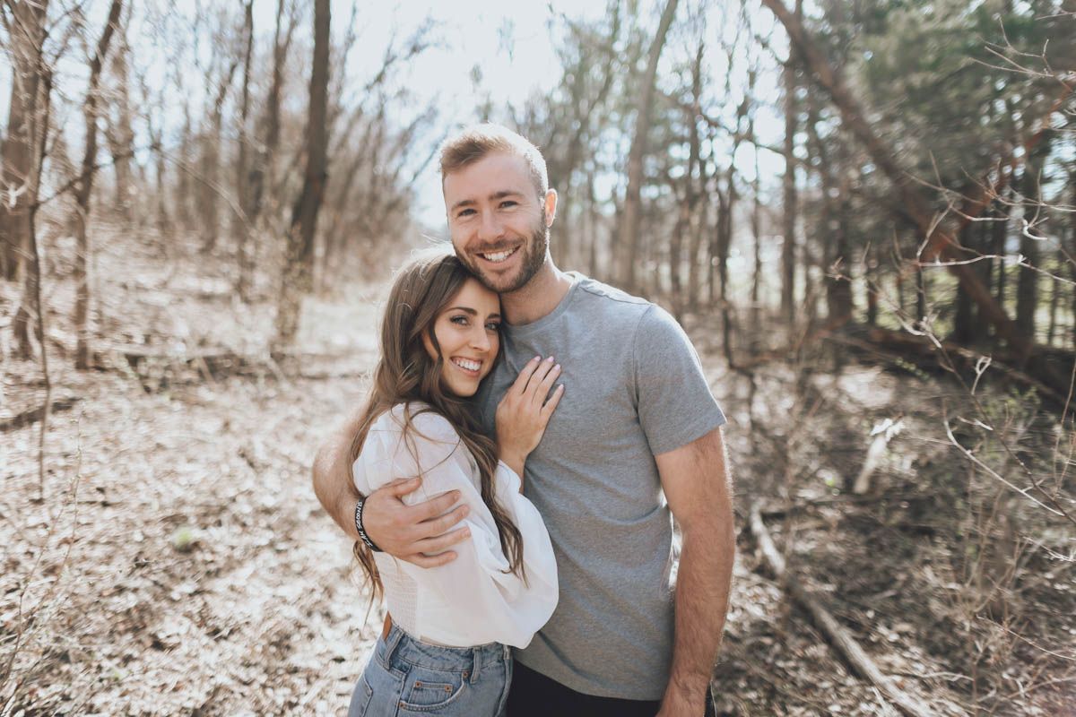 Romantic couple laughing and embracing while posing for casual photos in a forest setting.