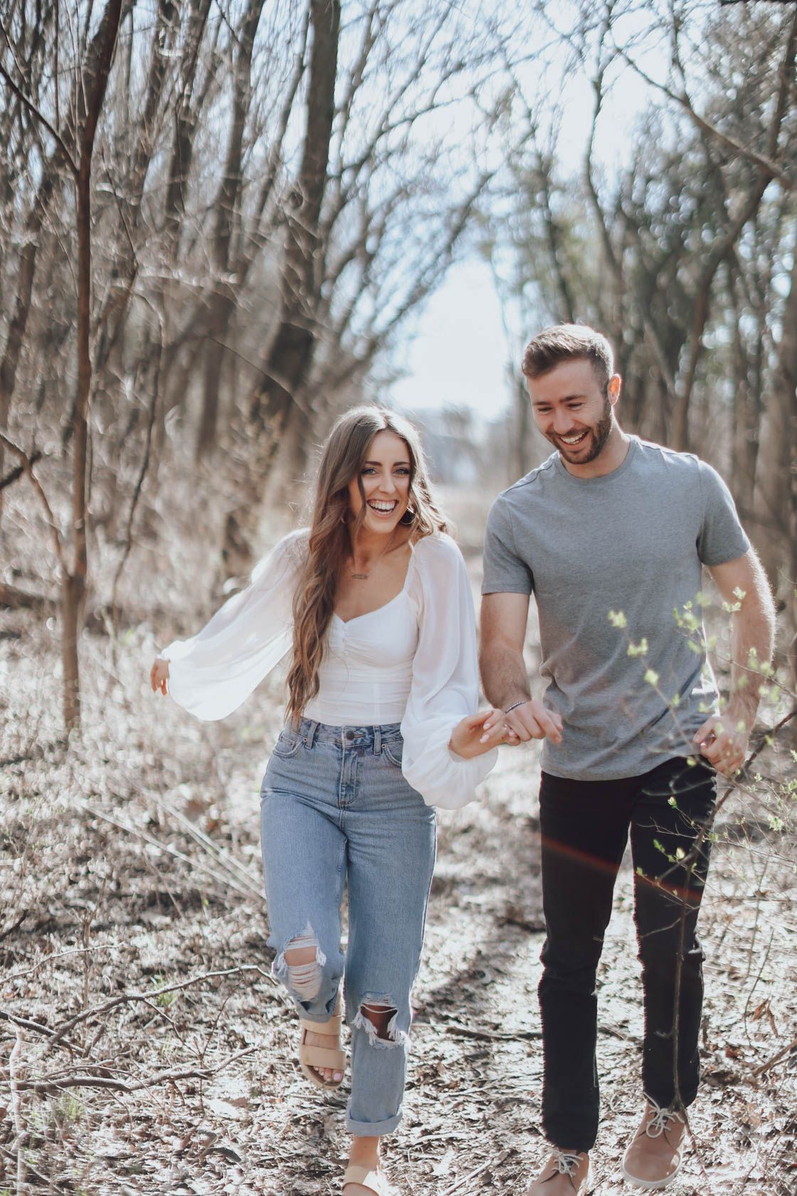 Playful couple running and laughing together through a winter forest landscape.