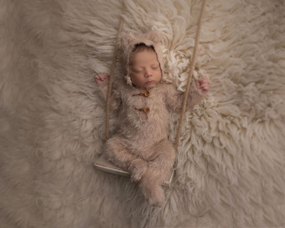 Newborn baby in lace outfit sleeping on cream fur swing prop.