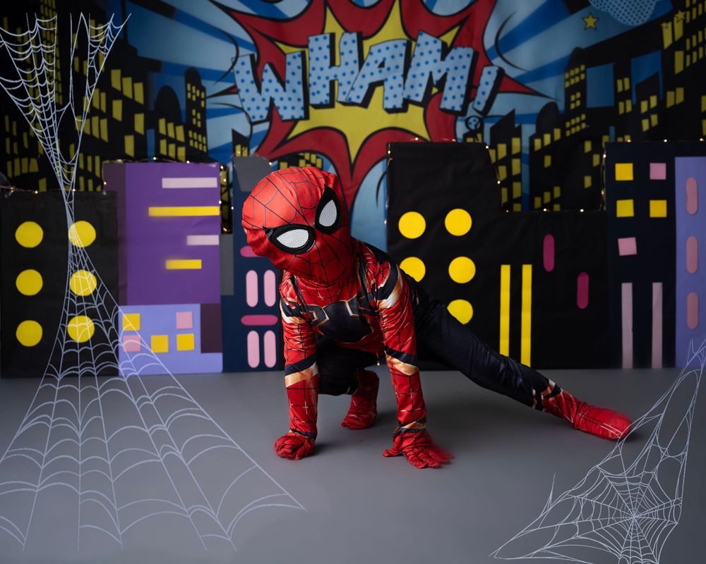 Small child in Spider-Man costume against comic book style city backdrop.
