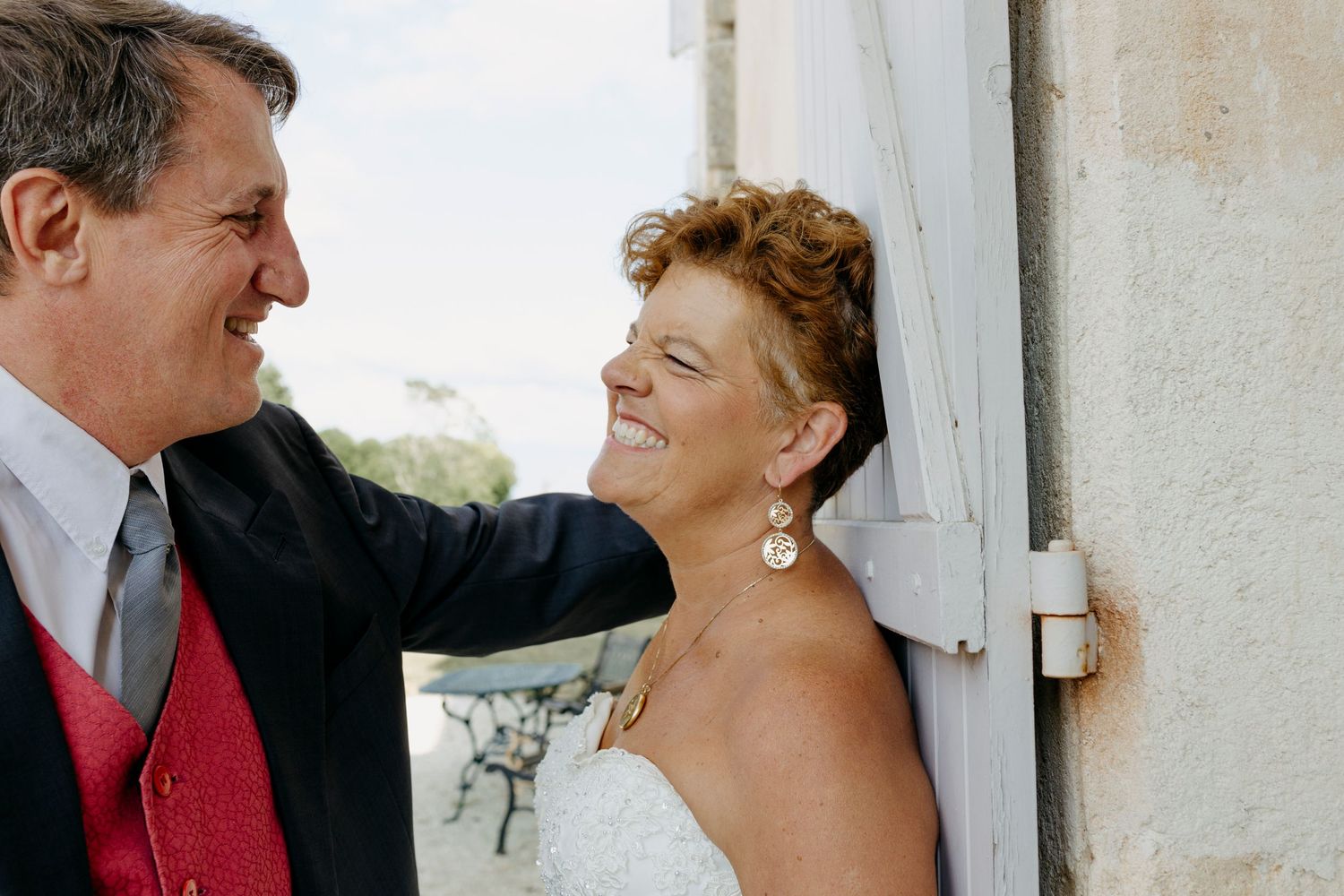 A couple shares a romantic moment against a white wall in formal attire.