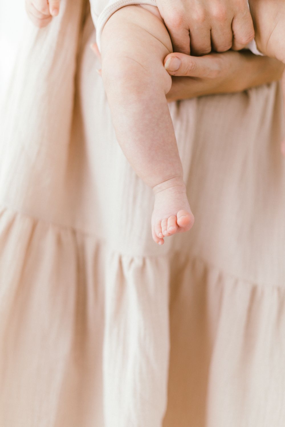 Close-up details of baby feet and flowing fabric in pale pink tones.
