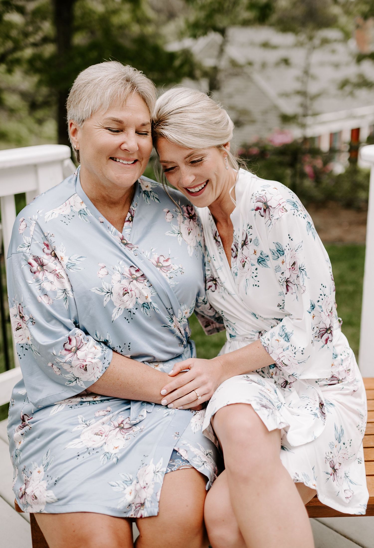 Two friends in matching floral robes share a candid moment on a porch swing.