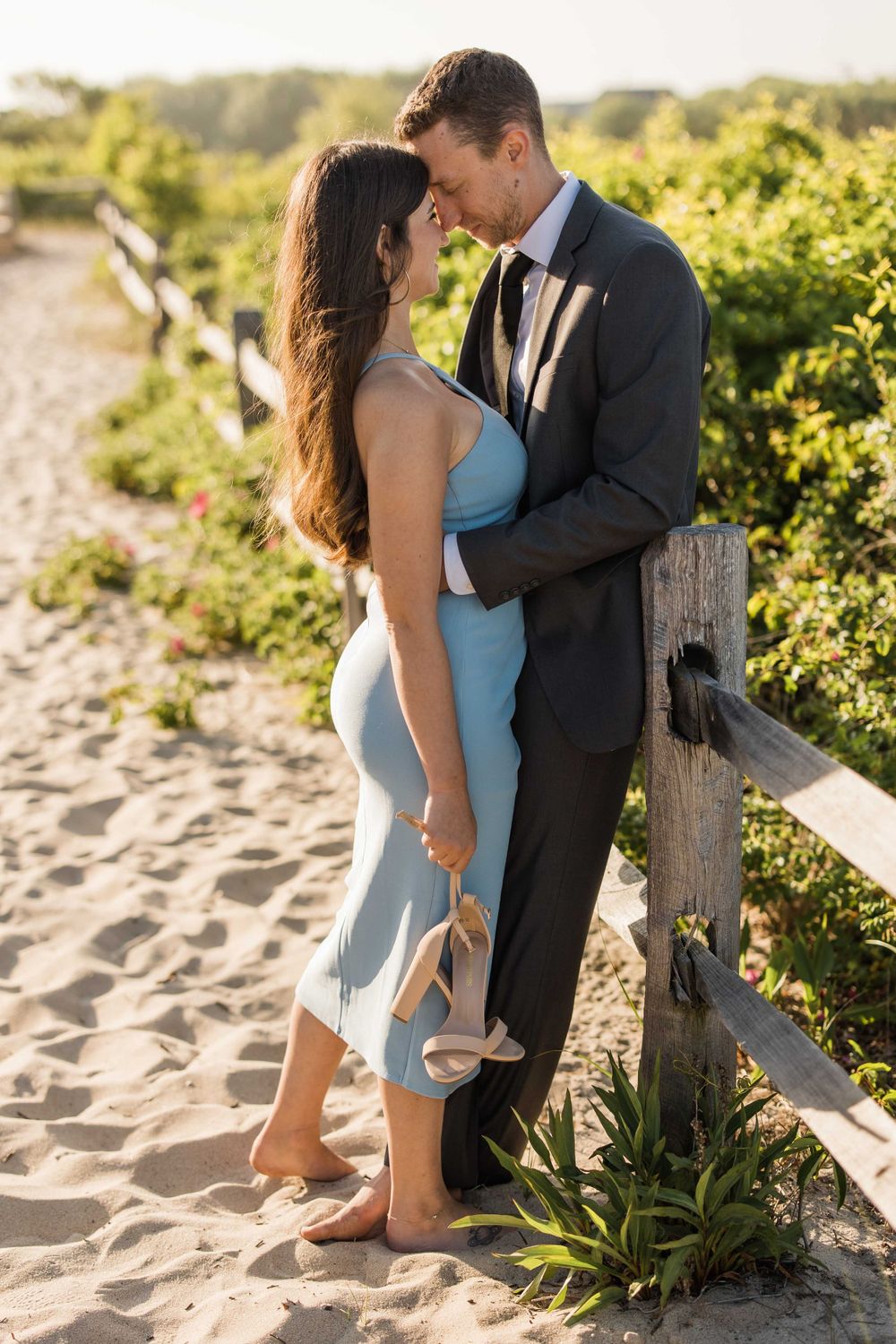 Romantic moment between couple in formal wear against wooden fence on sandy beach path.