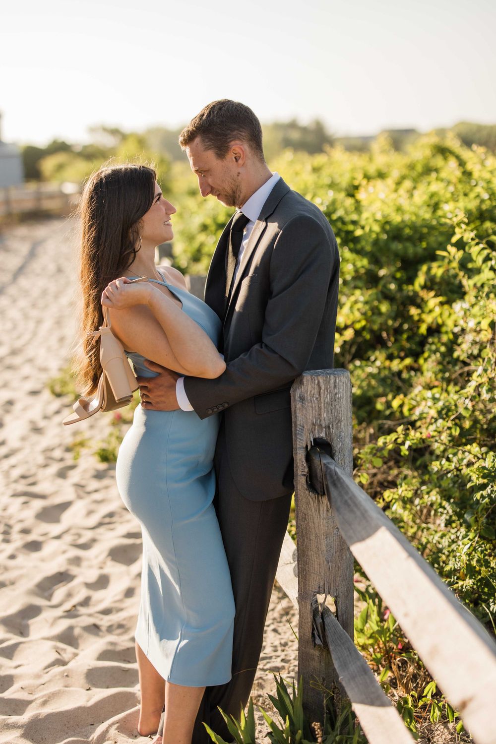 Intimate portrait of couple in formal attire embracing on beach path at golden hour.